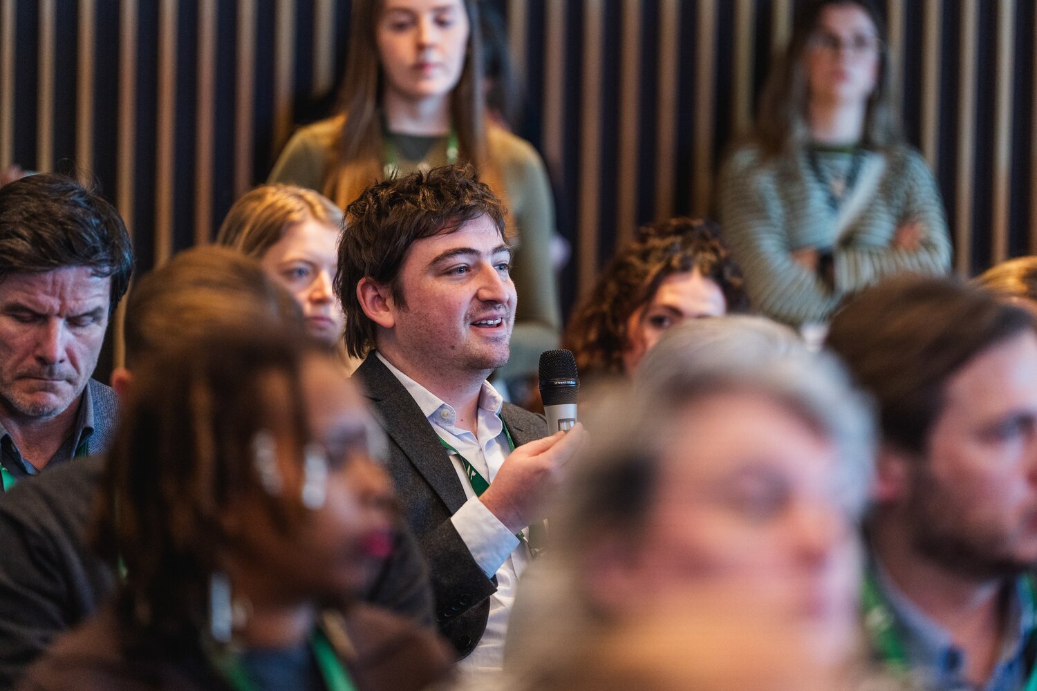 A person within an audience at a conference panel asks a question into a mic.